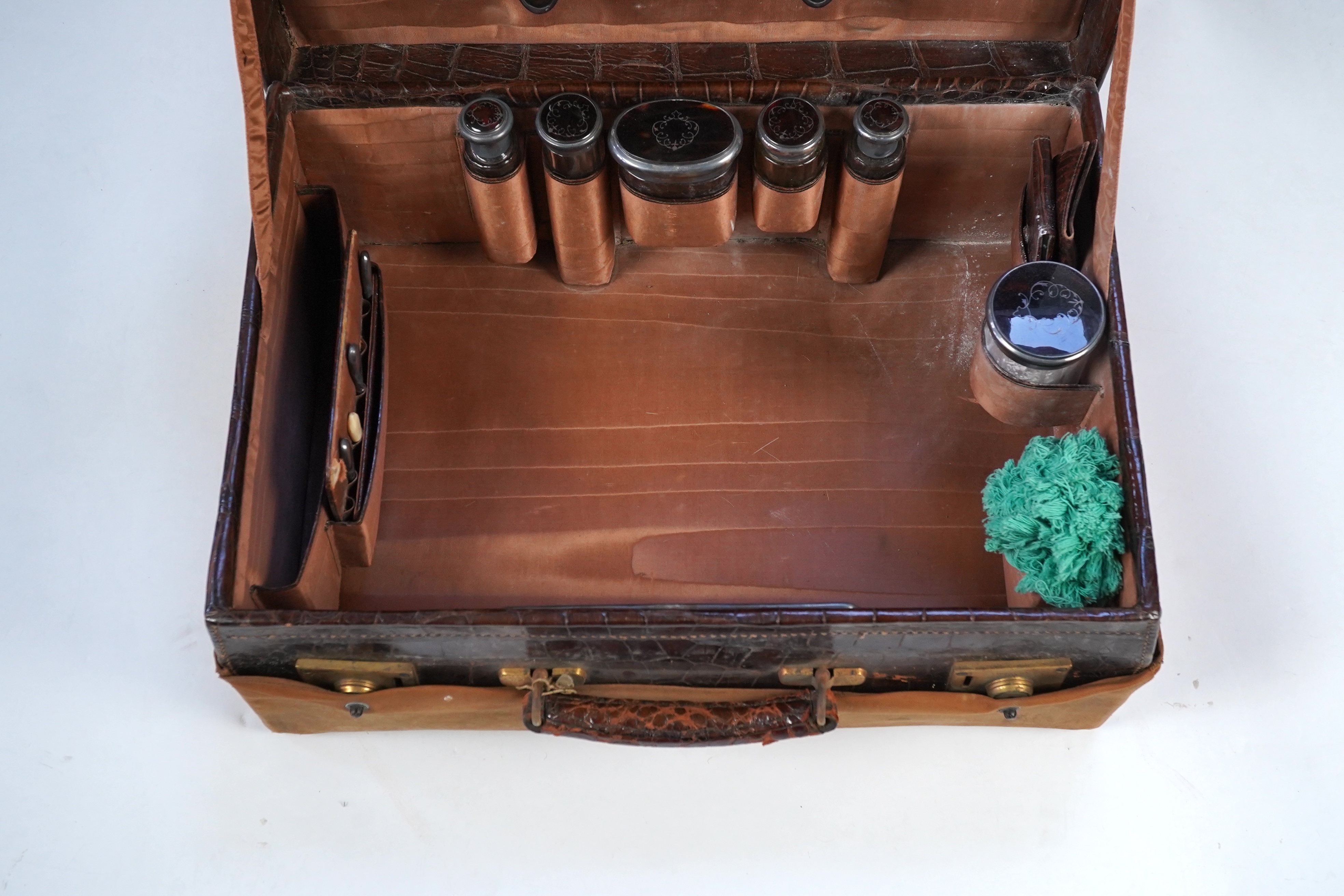 A George V crocodile skin travelling toilet case, containing twelve silver and tortoiseshell mounted accoutrements, by Collet & Anderson